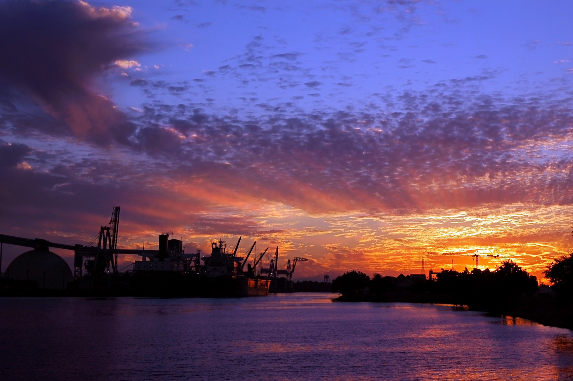 Cranes and a ship at the Port of Stockton silhouetted against a sunset